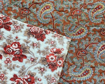 Puede incluir: Un primer plano de una tela con un patrón de paisley. La tela es marrón con acentos azules, amarillos y rojos. La tela está acolchada y tiene una textura suave.