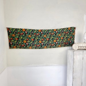 May include: A black tapestry with a floral pattern in shades of orange, yellow, green, and pink. The tapestry has a fringe border.