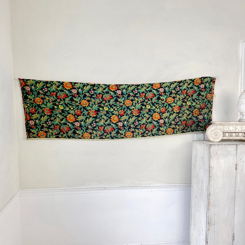 May include: A black tapestry with a floral pattern in shades of orange, yellow, green, and pink. The tapestry has a fringe border.