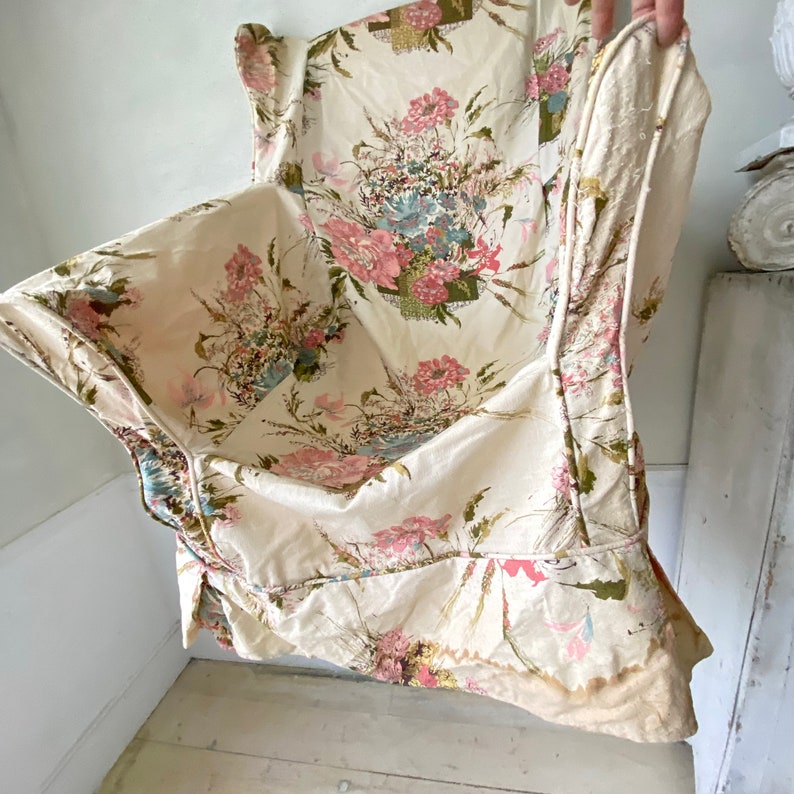 May include: A white floral fabric with pink and green flowers. The fabric has a ruffled edge and is folded in half.