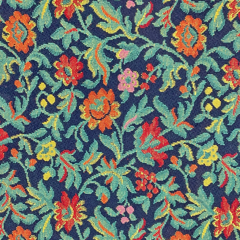 May include: A close-up of a fabric with a repeating pattern of blue, green, yellow, red, and pink flowers. The fabric has a textured woven look.
