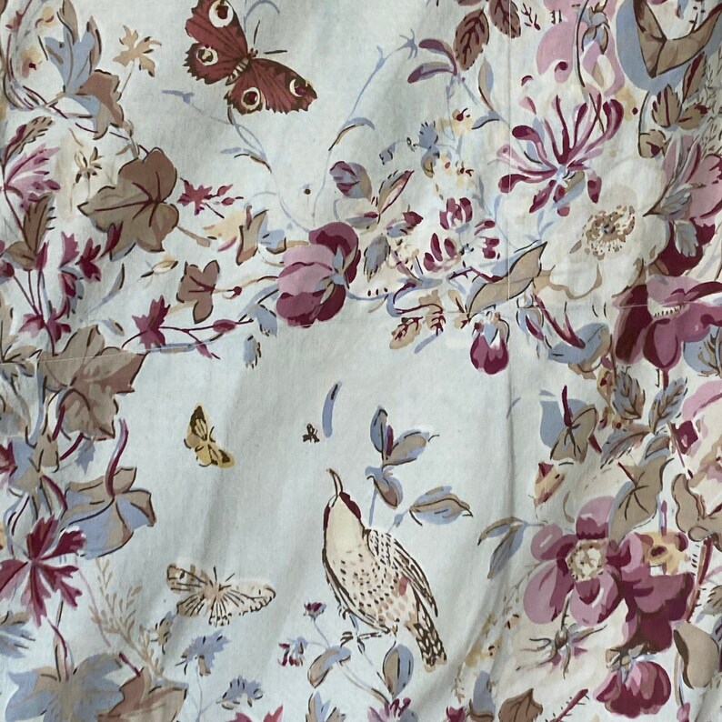 Puede incluir: Una tela blanca con un patr&oacute;n floral con flores rosas, marrones y azules, hojas y mariposas. Un peque&ntilde;o p&aacute;jaro est&aacute; posado en una rama.