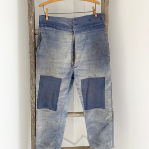 May include: A pair of light blue work pants with two large blue patches on the knees. The pants have a high waist and a button fly.