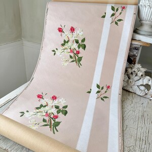 Op de afbeelding: Een rol vintage behang met een roze achtergrond en witte strepen. Het behang heeft een herhalend patroon van witte en roze bloemen.