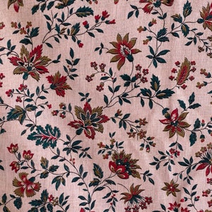 May include: A pink fabric with a repeating floral pattern. The flowers are red, green, and brown. The fabric has a subtle texture.