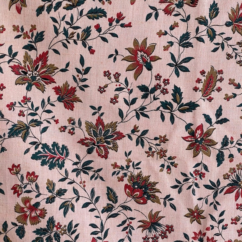 May include: A pink fabric with a repeating floral pattern. The flowers are red, green, and brown. The fabric has a subtle texture.