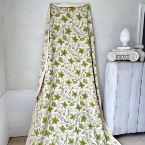 May include: A white fabric with a green grapevine pattern. The fabric is draped over a white surface.