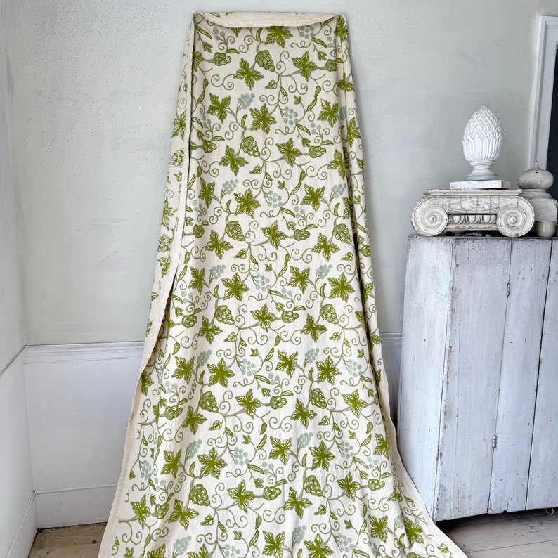 May include: A white fabric with a green grapevine pattern. The fabric is draped over a white surface.