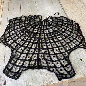 May include: Black lace shawl with a circular design. The lace is delicate and intricate, creating a spiderweb-like pattern.