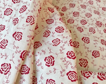 Könnte beinhalten: Cremefarbener Stoff mit einem sich wiederholenden Muster aus roten Rosen und grünen Blättern. Die Rosen sind stilisiert und gleichmäßig über den Stoff verteilt. Der Stoff ist gefaltet und zeigt das Muster aus verschiedenen Blickwinkeln.