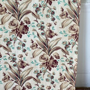Könnte beinhalten: Ein Vintage-Stoff mit einem sich wiederholenden Muster aus braunen und türkisfarbenen Blumendesigns. Der Stoff zeigt große, stilisierte Blumen mit Blättern und kleineren floralen Akzenten.