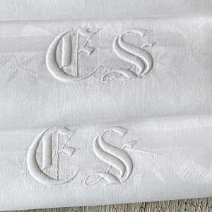 May include: Stack of white linen napkins with embroidered initials "ES" in a script font.