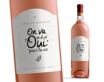 May include: A pink wine bottle with a white label that says "CUVÉE DU BONHEUR" and "On va se dire "Oui" pour la vie". The label also has a small heart and a branch with leaves.