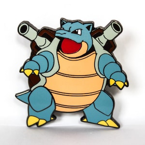 May include: A colorful enamel pin featuring the Pokémon Blastoise. The pin depicts Blastoise in shades of blue, tan, and yellow, with two cannons on its back. The pin has a black outline and a red mouth.