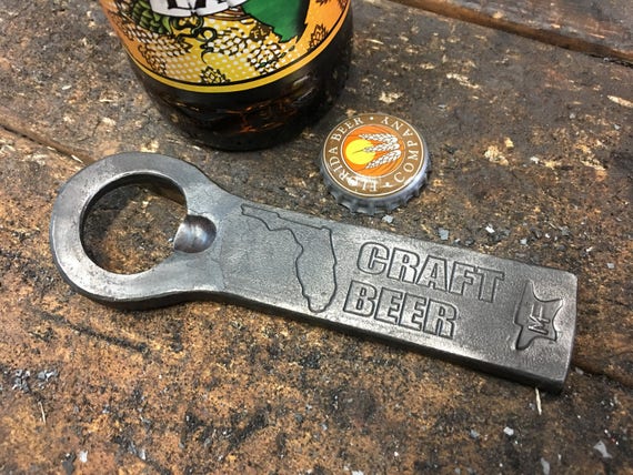 A blacksmith actually hammered this bottle opener into existence — the hammer marks, patina, and raw iron texture make it look like it was pulled from a Viking longhouse.