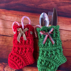 May include: Two crocheted Christmas stocking-shaped utensil holders. One is red with gold ribbon and a candy cane. The other is green with red and white plaid ribbon and a candy cane.