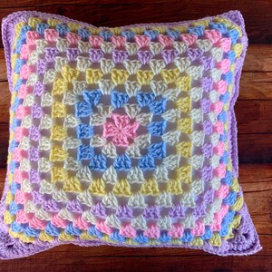 May include: A crocheted pillow with a granny square pattern in shades of purple, pink, yellow, and blue.