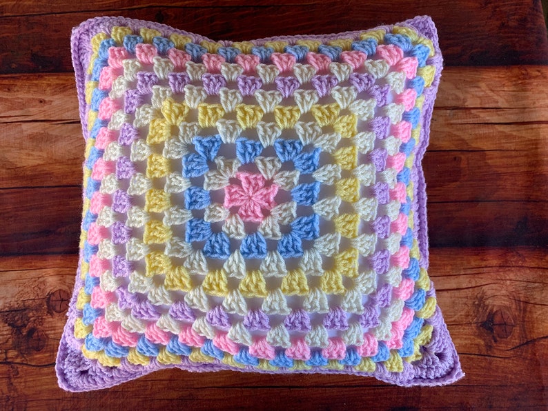 May include: A crocheted pillow with a granny square pattern in shades of purple, pink, yellow, and blue.