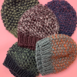 May include: Four knitted hats in different colors and patterns. The hats are made of a soft, textured yarn. The hats are arranged in a circle on a pink background.