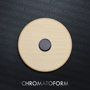 May include: A circular wooden item in a light hue, featuring a small, dark circular insert. The text "CHROMATOFORM" is shown in white at the base of the image against a dark backdrop.