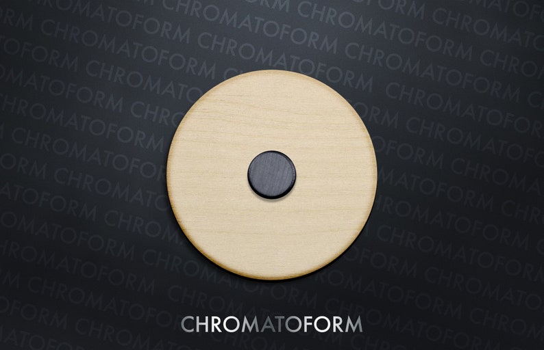 May include: A circular wooden item in a light hue, featuring a small, dark circular insert. The text "CHROMATOFORM" is shown in white at the base of the image against a dark backdrop.