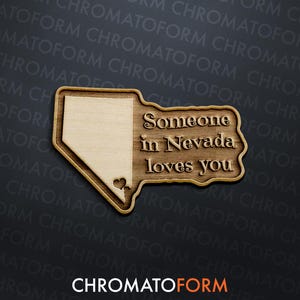 May include: Wooden plaque in the shape of Nevada with the text "Someone in Nevada loves you." The plaque has a light wood grain finish with a darker wood border and a heart detail. The background is dark gray.