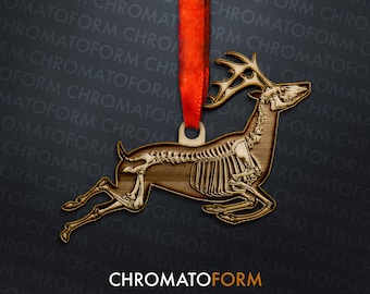 Puede incluir: Adorno de ciervo de madera con diseño de esqueleto, colgado de una cinta roja. El ciervo es marrón con una estructura ósea detallada. El adorno tiene un lazo para colgar. La palabra "CHROMATOFORM" está en la parte inferior.