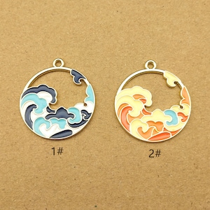 May include: Two gold-colored metal charms with a wave design. The charm on the left has blue, white, and black waves. The charm on the right has orange, yellow, and blue waves. Both charms have a hole at the top for attaching to a necklace or bracelet.