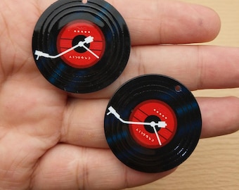 May include: Two black vinyl record-shaped charms with a red centre and white details. The centre has a clock design with white hands and the text "CAREFULLY". Each charm has a small hole at the top for stringing.