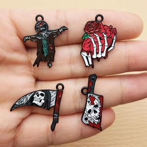 May include: Four Halloween-themed charms: a scarecrow, a heart with a rose held by a skeleton hand, a scythe with a skull flag, and a cleaver with a skull. Each charm has a black loop for attaching to jewelry or crafts.