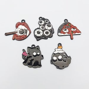May include: A set of five metal enamel charms featuring horror-themed designs: a mouth with an eyeball, a cluster of eyeballs, a slice of pizza with eyes, a black cat with wings, and a ghost-like figure with a small orange topper on its head.