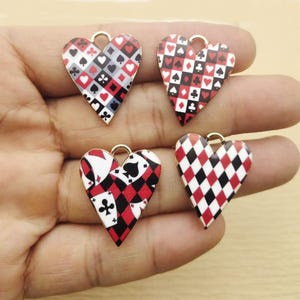 May include: Four heart-shaped metal charms featuring playing card suit patterns. The charms display red, black, white, and grey geometric designs, including diamonds, clubs, spades, and hearts, each with a small circular loop at the top for attachment.