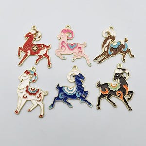 May include: Six metal charms shaped like leaping rams, each featuring colourful enamel fill and gold-toned outlines. The rams are depicted in red, pink, brown, white, blue, and black, with decorative patterns on their bodies and curled horns.