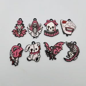 以下が含まれることがあります： 黒、白、ピンクのゴシックやホラーをテーマにしたデザインの金属製エナメルチャーム8個セット。チャームには、吸血鬼、翼のある骸骨、リボン付きの頭蓋骨、牙のある口、血を流すリンゴ、縫い目のあるウサギ、コウモリ、猫の骸骨が含まれています。