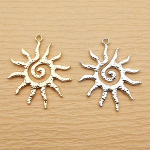 Peut inclure: Deux pendentifs en forme de soleil. L'un est de couleur or, l'autre est de couleur argent. Chaque pendentif présente un centre en spirale et des rayons pointus s'étendant vers l'extérieur. Les pendentifs ont une petite boucle en haut pour l'attacher.