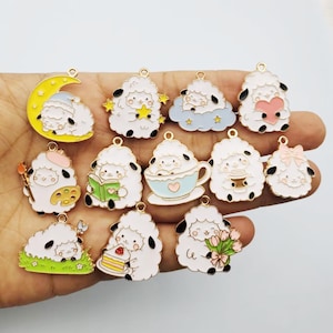 May include: A collection of twelve metal enamel charms featuring white sheep in various activities, including sleeping on a yellow moon, holding a star, sitting in a blue cloud, holding a pink heart, painting, reading, drinking from a cup, and holding flowers.