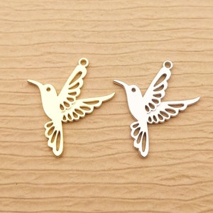 May include: Two metal hummingbird charms, one gold and one silver, with intricate cut-out designs. The charms are ideal for jewellery making or crafting projects.