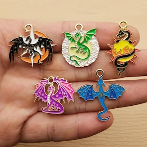 May include: A collection of five dragon-themed pendants in various colors. Each pendant features a different dragon design, including a black and white dragon on a crescent moon, a green dragon, and a purple dragon with pink wings. All pendants have a gold-colored loop.