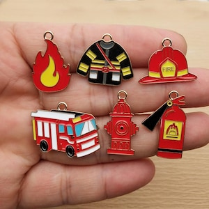 Peut inclure: Une collection de breloques en émail colorées sur le thème des pompiers. Les breloques comprennent un camion de pompiers rouge, une borne-fontaine, un extincteur, une veste de pompier, un casque avec le texte "FIRE" et une flamme.