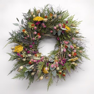 K&ouml;nnte beinhalten: Ein kreisf&ouml;rmiger Kranz aus verschiedenen getrockneten Blumen und Gr&uuml;nzeug. Der Kranz hat eine Basis aus gr&uuml;nen Bl&auml;ttern, akzentuiert mit gelben, rosa und orangefarbenen Bl&uuml;ten. Getrockneter Weizen und Eukalyptusbl&auml;tter sind ebenfalls enthalten.