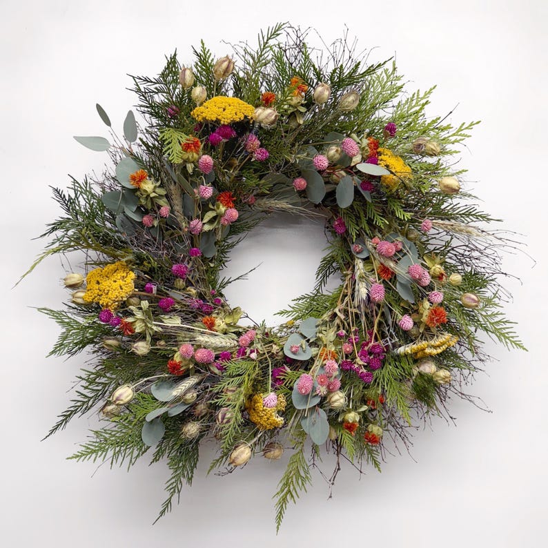 K&ouml;nnte beinhalten: Ein kreisf&ouml;rmiger Kranz aus verschiedenen getrockneten Blumen und Gr&uuml;nzeug. Der Kranz hat eine Basis aus gr&uuml;nen Bl&auml;ttern, akzentuiert mit gelben, rosa und orangefarbenen Bl&uuml;ten. Getrockneter Weizen und Eukalyptusbl&auml;tter sind ebenfalls enthalten.