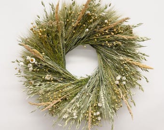 Könnte beinhalten: Ein runder Kranz aus getrockneten grünen Gräsern, Weizenhalmen und Haferstängeln, akzentuiert mit kleinen weißen Blüten und goldenen Samenkapseln. Das Arrangement zeichnet sich durch eine Vielzahl von Texturen und Naturtönen aus.