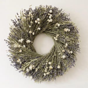 May include: A circular wreath constructed from dried lavender stems and small white strawflowers. The arrangement features a dense, textured composition of purple lavender buds and delicate white blossoms, creating a natural, botanical display.