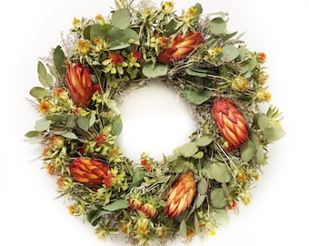 May include: A dried flower wreath with a variety of green leaves, orange and red flowers, and a circular shape.