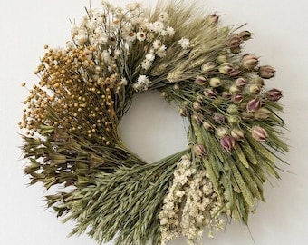 May include: A circular wreath composed of dried flowers and grasses. The wreath features a variety of textures and colors, including shades of brown, green, and white. The arrangement is symmetrical and appears to be handmade, suitable for home decor.
