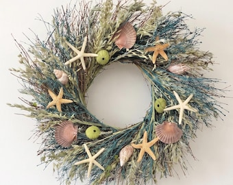 May include: A circular wreath constructed from thin brown twigs, blue-dyed branches, and dried grasses. The wreath is decorated with several white and tan starfish, various pink and white seashells, and small, round, textured green sea urchins.
