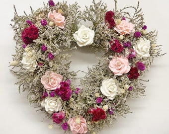 May include: Heart-shaped wreath composed of dried greenery, white, pink, and burgundy flowers. The wreath features a variety of textures and colors, creating a natural and romantic aesthetic. Ideal for home decor or special occasions.