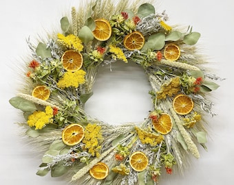 May include: A dried floral wreath with a mix of dried grasses, wheat, and eucalyptus leaves. The wreath is decorated with dried orange slices and small yellow flowers.