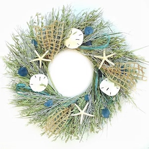 May include: A green, brown, and blue wreath with seashells, starfish, and netting. The wreath is made of dried grasses and is perfect for a coastal or nautical theme.