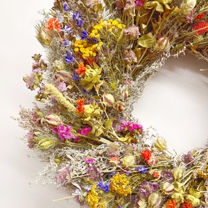 May include: A dried flower wreath featuring a mix of colours, including yellow, orange, pink, purple, and blue. The wreath is crafted from dried flowers and grasses, ideal for bringing a touch of natural beauty to any home.